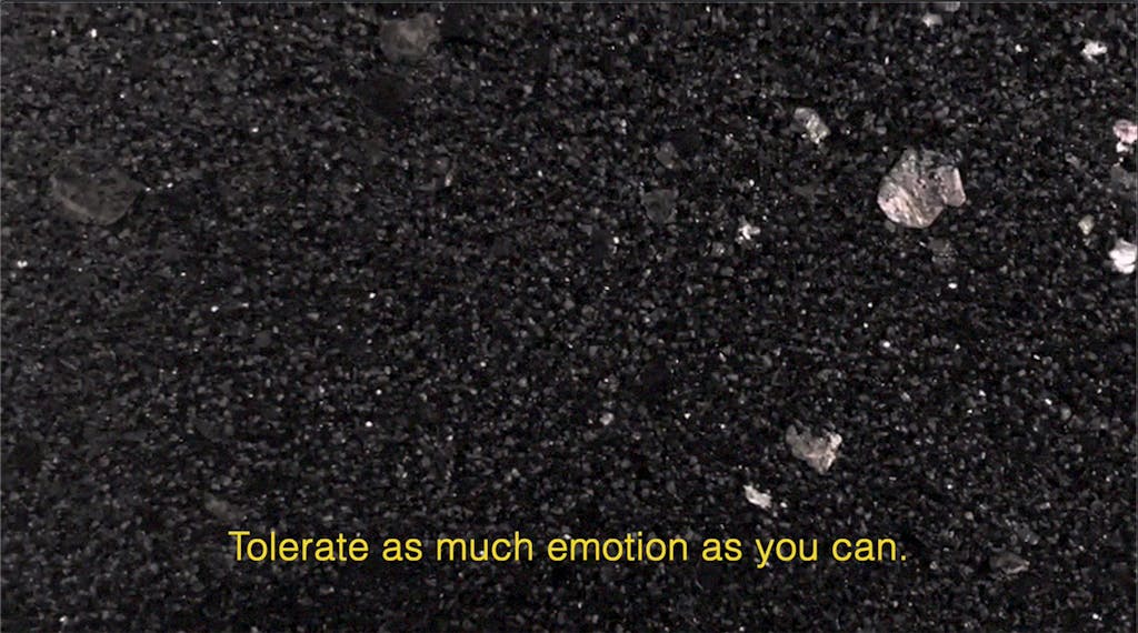 [An asphalt black and sparkled mica ground hosts a line of yellow open captions that read: "Tolerate as much emotion as you can."] - © Galerie Max Mayer and the artists, Paris Internationale